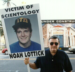 Dr. Edward Lottick with sign that says: victim of $cientology - Noah Lottick
